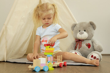 Toddler girl playing with wooden train made from wooden blocks - educational toys for preschool and kindergarten child. 