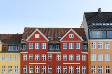 Fototapeta na wymiar Colorful houses in yellow, red and orange of the Nyhaven in Copenhagen Denmark photographed frontally on a sunny day with a bright blue sky.