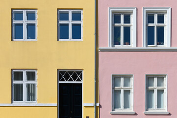 Colorful houses in yellow and pink of the Nyhaven in Copenhagen Denmark photographed frontally on a sunny day with a bright blue sky.