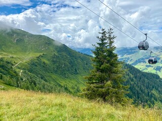 View towards Saalbach village and mountains in Saalbach-Hinterglemm skiing region in Austria on a beautiful summer day with cableway and lush meadows used by cows for grazing.