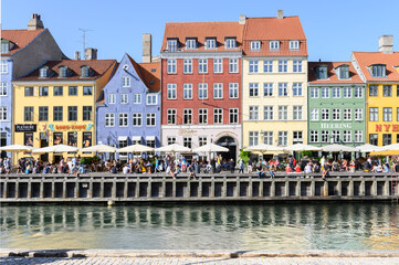 COPENHAGEN, DENMARK 29. June 2019: People relax on a promenade along Nyhavn in front of a row of colorful houses on a warm summer's day.