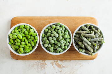 Frozen vegetables such as green peas, soy, green beans and baby in white bowls top view. Healthy food, frozen food