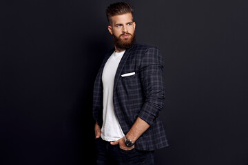 Handsome man with perfect hairdo and beard looking away while standing against black background
