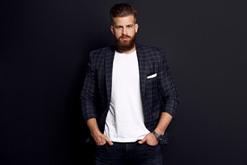 Obraz premium Handsome man with perfect hairdo and beard looking at camera while standing against black background