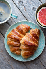 Top down view of a breakfast including fresh, golden and flaky homemade crescents on a colourful plate with coffee and grapefruit