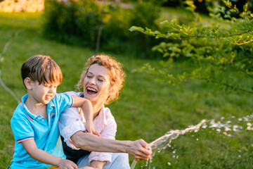 Little boy and happy mother gardener watering garden with hose