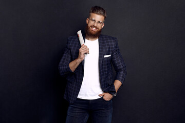 Handsome young man in smart casual wear holding newspaper and looking at camera while standing against black background