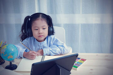 Portrait Asian kid girl wearing headphones looking at the tablet for learning education distance...