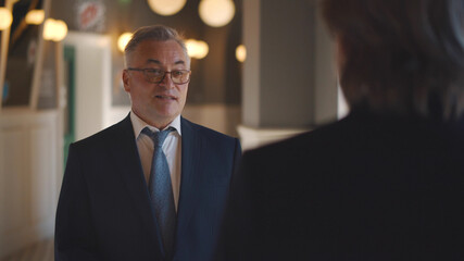 Fototapeta premium Back view of successful senior businessman talking to partner while waiting in lobby