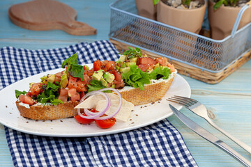 A large sandwich with avocado, tomato, basil and cheese spread. Toast on white baguette bread. Close-up still life on the table. Sandwich food snack and snack. Healthy diet. Sesame and flax seeds.