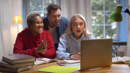 University students studying together looking at laptop screen and celebrating academic success