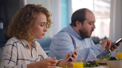 Obraz premium Couple using smartphone having breakfast in cozy kitchen at home