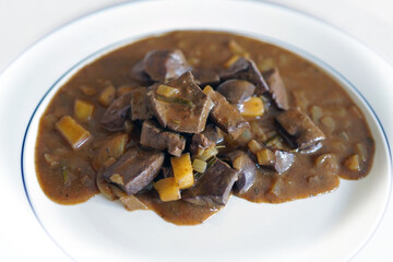 ready to eat, liver, heart and kidneys from a roe buck in sour sauce with onoins and apple on a white plate