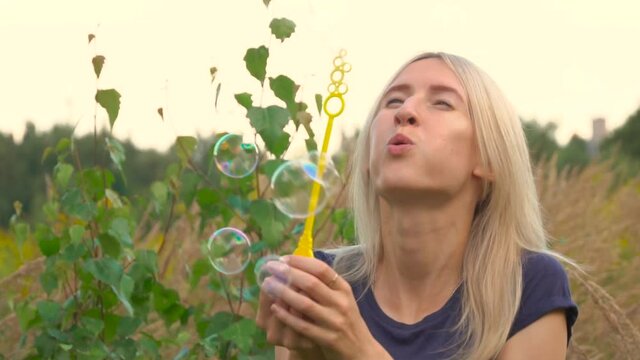 A young woman blows bubbles in nature. A happy young blonde is walking in the Park and blowing soap bubbles on a Sunny day.
