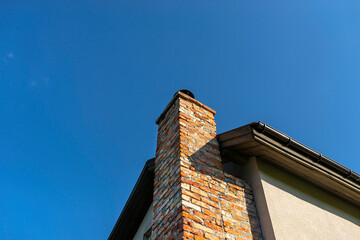 A red ceramic brick chimney standing at the rear of the building, by the facade, with a blue sky in the background.