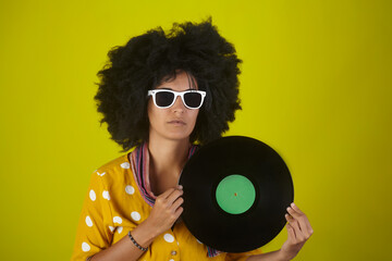 Beautiful girl with afro curly hairstyle holding an LP record on yellow background