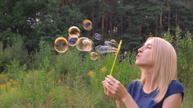 A young woman blows bubbles in nature. A happy young blonde is walking in the Park and blowing soap bubbles on a Sunny day.
