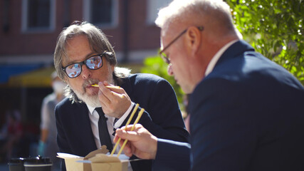 Close up of two successful aged business partners having lunch together in outdoors cafe