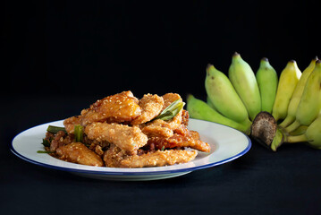 Fried banana mix sesame and pandan leaf for aroma (Thai called Kluay Thod) in white dish and Banana on black cloth background Thai snack