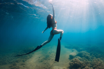 Slim woman freediver posing  underwater in blue sea with sun rays. Freediving with fins in ocean