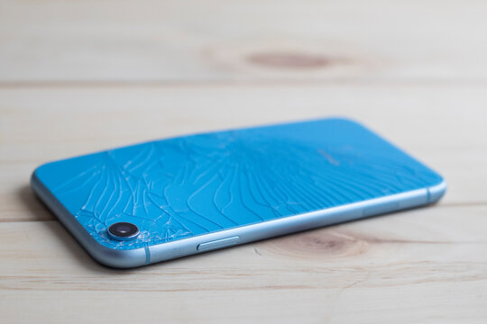 Cracked broken back from glass of modern blue smart cell mobile phone on the floor. Repair, service concept