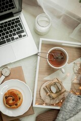 Breakfast. Laptop, mug of hot tea, bun, candle, eucalyptus in a vase. Cozy autumn. Home.