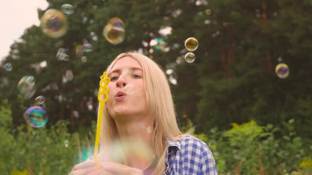 A young woman blows bubbles in nature. A happy young blonde is walking in the Park and blowing soap bubbles on a Sunny day.