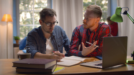 Cool students studying with books and laptop in dorm living room