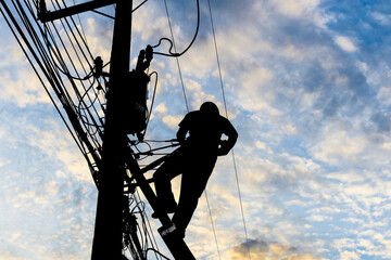 Silhouetted electricians working at electric pole in blue sky background.