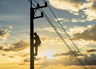 Silhouette man works with electricity on a pole with the sunset in the sky. - obrazy, fototapety, plakaty