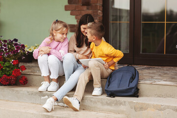Obraz premium A group of happy teenage children after school sit on the steps and play on a digital tablet. Modern children, digital technologies