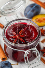 Jar with homemade plum jam with cinnamon and star anise on a white wooden background close-up. Fresh fruit with spices on the table. Selective focus