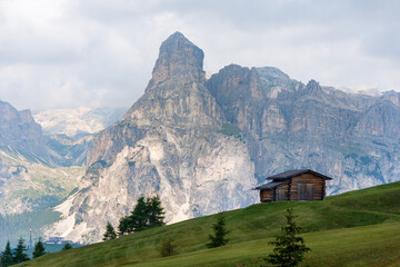 Isolated mountain hut surrounded by green meadows during summer. High Dolomite peaks of Italian Alps are visible in the background. Val Badia - South Tyrol, Italy