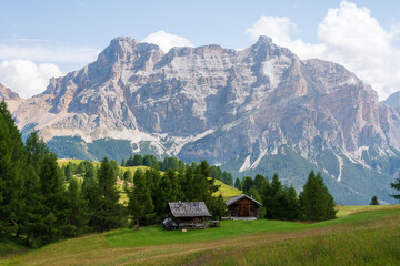Obraz premium Isolated mountain huts surrounded by green meadows during summer. High Dolomite peaks of Italian Alps are visible in the background. Val Badia - South Tyrol, Italy