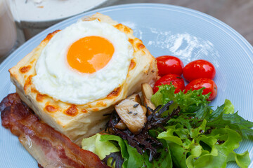 Ham and cheese sandwich with bechamel sauce and topped with a fried egg, known as Croque-madame. Croque madame sandwich on the table. Hot french toasts with ham, melted emmental cheese and fried egg.
