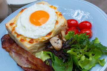 Ham and cheese sandwich with bechamel sauce and topped with a fried egg, known as Croque-madame. Croque madame sandwich on the table. Hot french toasts with ham, melted emmental cheese and fried egg.
