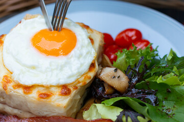 Croque madame delicious breakfast with ham, cheese, egg and spinach with vegetables. Cut fried egg on Croque madame, ham and cheese closeup on the plate. Eating croque-madame with beautiful fried egg.