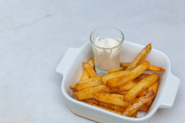 Crispy Potato French Fries in white bowl. French fries with dip sauce closeup on the table. Homemade Baked Potato Fries with Mayonnaise on white bowl. Close up Tasty Fried potato snacks in bowl.