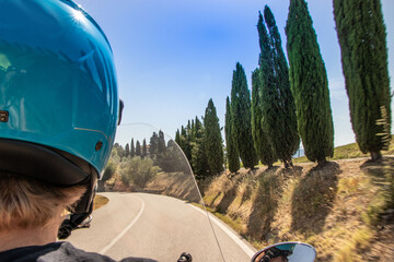 A guy drives a scooter in the streets among the cypresses of the Tuscan hills
