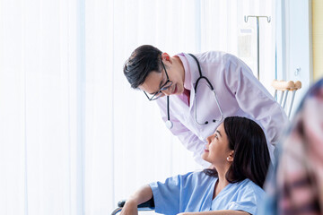 Naklejka premium Positive doctor and patient on wheelchair. Female patient being pushed in Wheelchair by Young doctor. Doctor talking to young female patient on wheelchair visiting doctor for regular check.