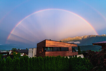 Rainbow over modern copper building in Austrian alp mountains village during sunset, Wildermieming,...