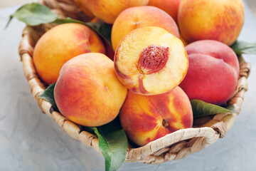 Ripe peaches in a wicker basket on a stone gray table with a juicy peach slice with a stone pit.