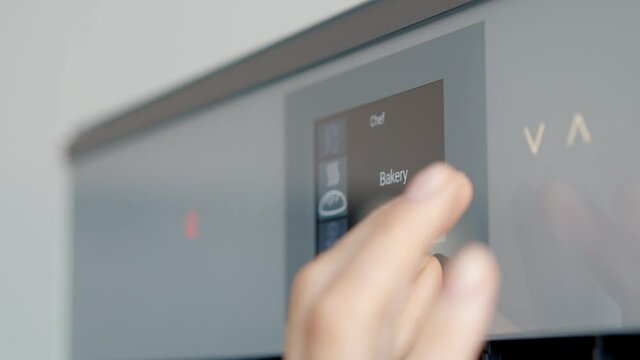 Close up of woman touching sensor button on electric oven in kitchen