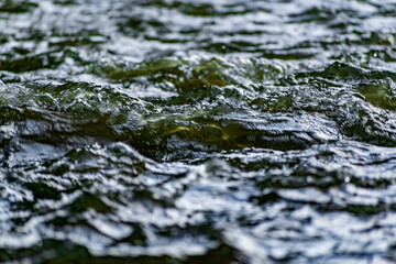 Fresh water in motion, swirling current with flying spray. Green tint on the light, transparent liquid in the river, like small waves for background and texture