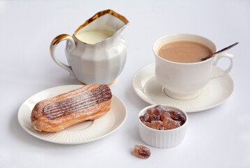 White cup of coffee, cake on a plate, brown sugar and milk on a white background