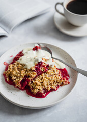 Plum crumble on white plate with coffee. Autumn and winter comfort food, cosy atmosphere, nordic style