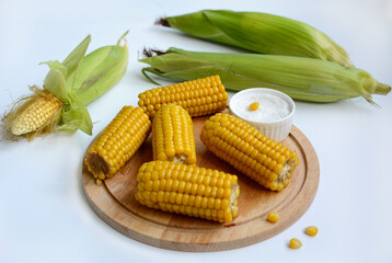Ripe juicy corn, salt on a wooden plate on a white background.
