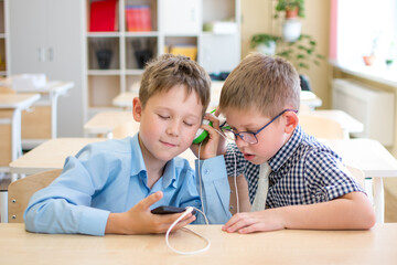 Two students at a Desk listen to music from the same headphones.