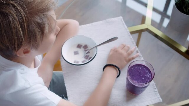 Cute young little boy eating breakfast in kitchen with milk in cereal bowl. Kid eating self-made breakfast with healthy smoothie at home.
