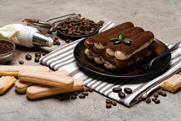 Classic tiramisu dessert and savoiardi cookies on ceramic plate on concrete background